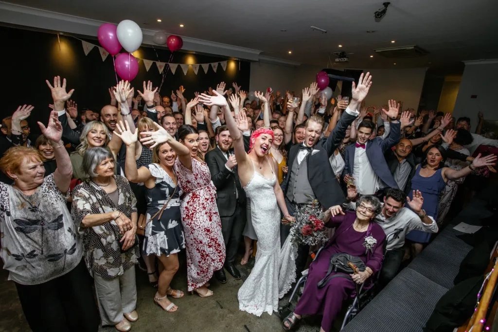 Large wedding group inside a spacious function venue in Richmond waving at the camera